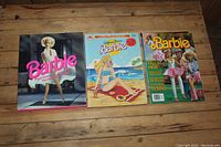 Shows all three Barbie books and magazines side by side on a wooden surface for lot overview
