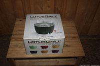 Sealed boxed LotusGrill charcoal grill with printed product branding and color options.