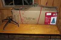 Photo of boxed blue spruce artificial Christmas tree with metal stand on table in wooden room.