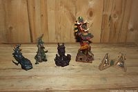 Five miniature dragon figurines displayed on wooden surface against wooden panel backdrop.