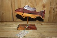 Front view of wooden fish sculpture showing carved details, natural wood grain, and painted eyes on a wooden stand.