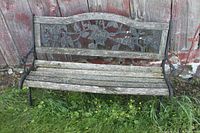 Front view of a weathered garden bench showing the full metal frame with floral design on the backrest and wooden slat seating area.