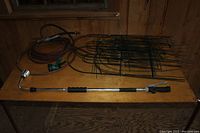 Photo showing gardening hose, spray nozzle, watering wand and green metal plant fences on a wooden surface.