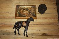 Horse-themed items on wooden surface showing a leather horse figurine, a framed relief carving, and a dark horse plaque.