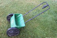Full view of the green Scotts lawn spreader showing hopper, wheels, and black handle with trigger lever