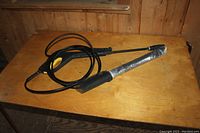 Full view of pressure washer wand coiled with hose on a wooden surface.