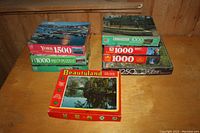 Photo of stacked jigsaw puzzle boxes showing variety of brands and piece counts including 1500, 1250, and 1000 pieces