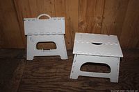 Two white plastic folding step stools shown folded and unfolded against a wood background.