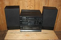 Full front view of Panasonic stereo system stacked with two black speakers on either side on wooden surface and wood wall background.