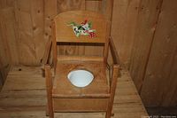 Front view of vintage wooden potty chair showing painted design and ceramic bowl