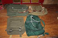 Overview photo of all four vintage ranger bags laid out on wooden floor, showing various colors, materials, and strap closures.