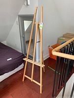 Full view of the wooden Tri-bois art easel standing upright near bed and staircase.