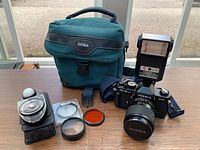 Photo showing Yashica FX-3 Super 2000 camera with 35-70mm lens, CS-220 flash, Sekonic L-398M light meter, three filters, and Sigma soft case on table.