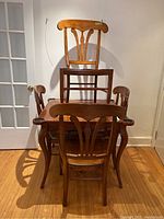 Four chairs arranged around and stacked on a small wood game table.