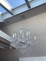 Full view of chandelier hanging from ceiling chain beneath skylights, showing eight arms and candle-style bulbs