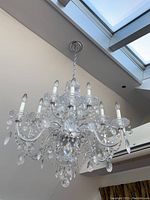 Front side view of large lucite and glass chandelier featuring multiple arms with candle bulb holders and numerous hanging crystal drops, shown hanging from ceiling chain.
