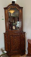 Front angled view of the full corner cabinet showing the glass front upper section and wood lower compartment with floral inlaid details.