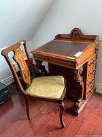 Front view of wooden writing desk and matching chair showing leather top and carved wood details