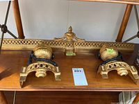 Photo showing two matching decorative metal finials and one wider finial piece on a wooden shelf shelf.