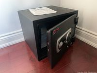 Black Uscan floor safe with open door showing interior space and paper on top.