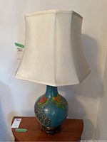 Full view of lamp showing porcelain body, carved wood stand and fabric shade