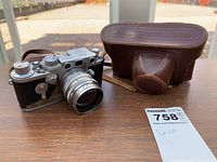Camera body with collapsible lens and leather case next to MaxSold tag