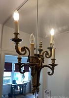 Two brass wall sconces mounted on wall, one missing finial, both lit with three bulbs each.