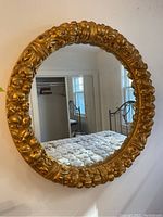 Full frontal view of round mirror and ornate frame against wall reflecting bedroom