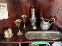 Full grouping of six ornate metal pieces and two goblet cups displayed on wooden surface