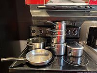 Overview of multiple stainless steel sauce pans including stacked ones, frying pan, and Dutch oven on stove