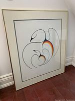 Full view of the framed print leaning against wall, showing abstract swan design with color gradients and gold metal frame.