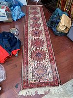 Full length of handwoven cotton runner rug laid out on a wooden floor showing geometric patterns and fringes at one end.