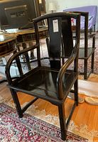 Left-front angle view of one black wood armchair with curved arms and straight legs on a patterned carpet, showing seat and backrest.