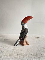 Full front and side view of the carved and glazed pottery toucan figurine showing large orange beak, detailed painted feathers, and posture on ceramic base.