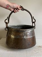 Front angled view of hammered metal cauldron with handle held up showing size and shape.