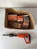 Full lot including Ramset powder actuated nailer and multiple boxes of nails and fasteners in a cardboard box.
