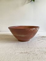 Side view of the large pottery bowl showing the wide top opening, smooth reddish-orange glaze with tan speckles, and slightly flared lip.