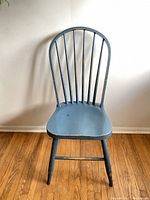 Front view of a single blue wooden dining chair showing spindle back and contoured seat with some paint wear.