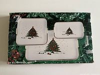 Photo showing the set of three vintage nesting Christmas serving trays in original packaging with visible damage on largest tray corner