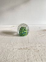 Front view of round glass paperweight with controlled bubbles and colorful swirl inside