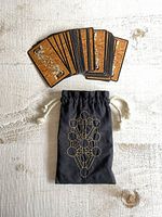 Tarot card deck fanned out showing card backs and black drawstring bag with gold embroidery.
