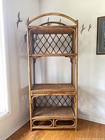 Full view of the tall bamboo and wicker shelving unit showing all four shelves, lattice back panels, and curved top arch.