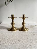 Pair of vintage brass candle holders shown side by side on white surface, clear view of their height, shape, and polish.