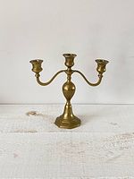 Front view of vintage brass three candle stick holder on a white wooden surface.
