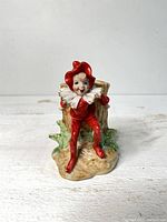 Front view of red pixie elf planter showing figure seated next to log holder on textured base.