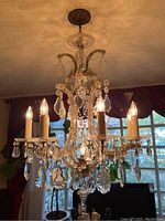 Full view of hanging chandelier showing six lit bulbs, draped crystal drops and ceiling canopy