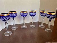 Six cobalt blue cut crystal wine glasses with gold trim arranged in a row