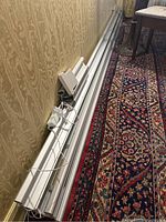 Multiple straight aluminum rail sections with integrated gear rack and white power supply unit laid along wall over carpet.