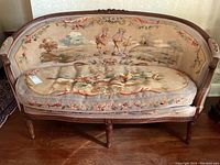 Front view of settee showing curved back, cushion and pastoral needlepoint scene.