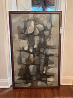 Full view of the framed abstract painting leaning against wall